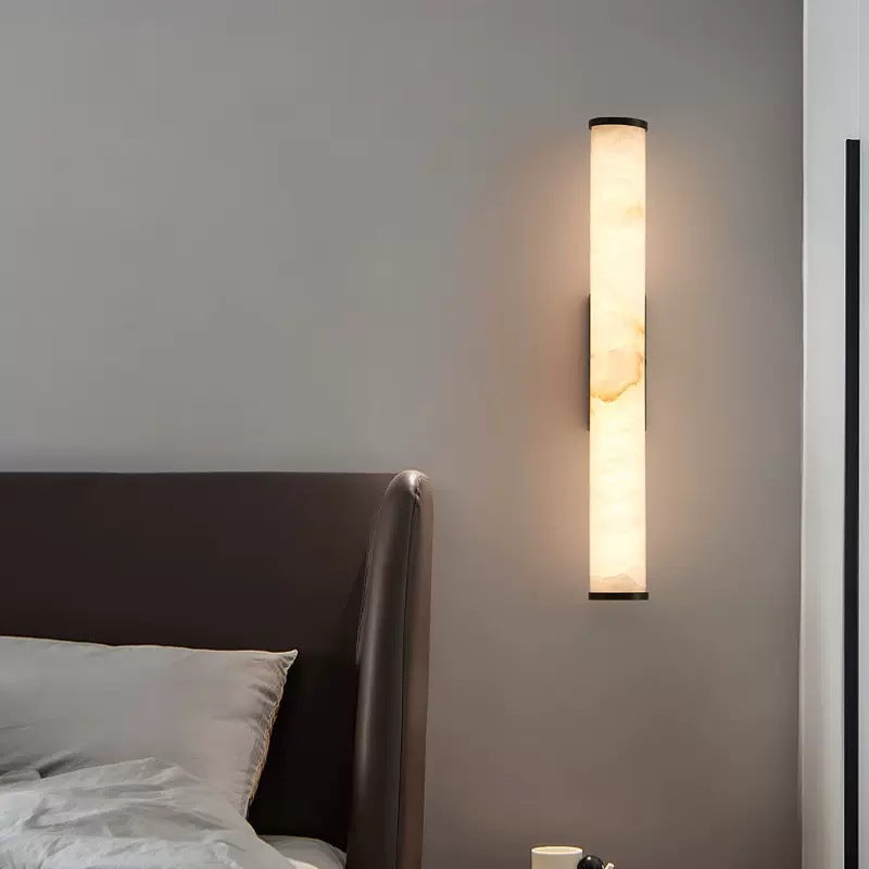 Alabaster stone aerq wall light acting as a luxurious ambient bedside lamp next to a dark headboard