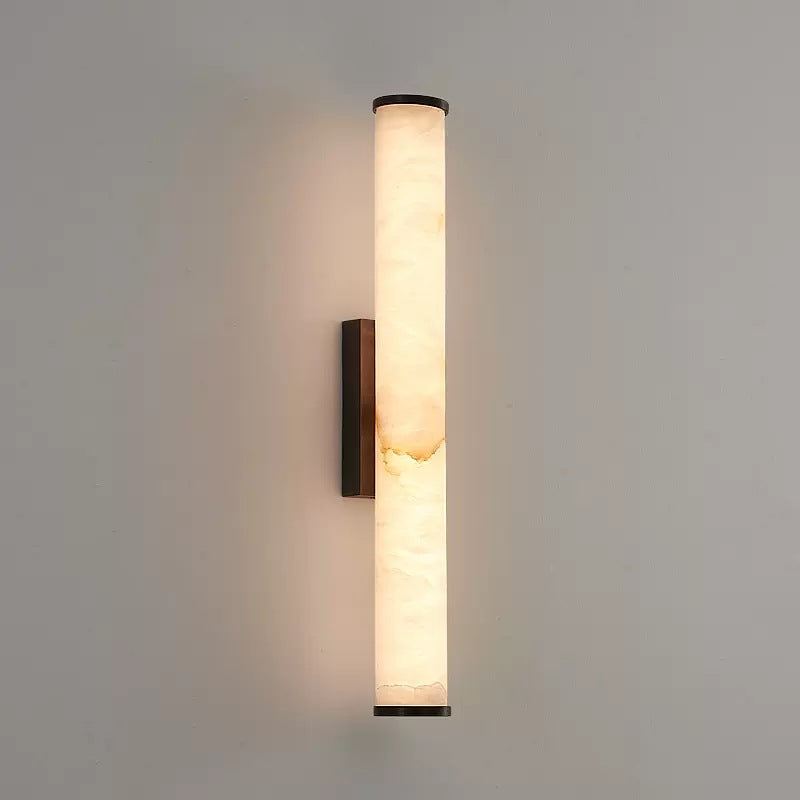 Vertical alabaster aerq tube sconce with sleek black hardware glowing warmly on a plain neutral wall
