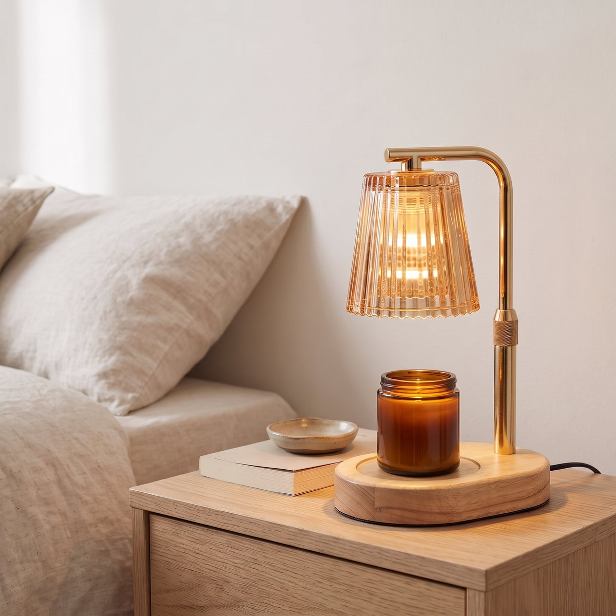 Ambra amber ribbed glass candle warmer lamp warming a candle jar on an oak bedside table next to a bed with linen bedding