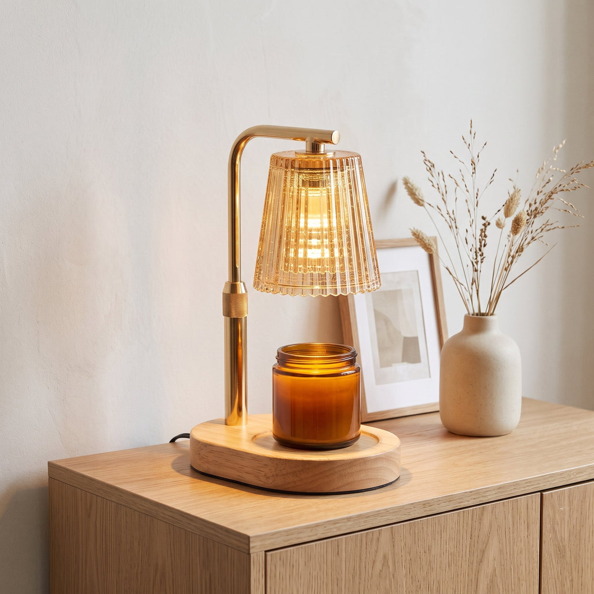 Ambra amber ribbed glass candle warmer lamp warming a candle jar on an oak sideboard with dried grasses and a framed print