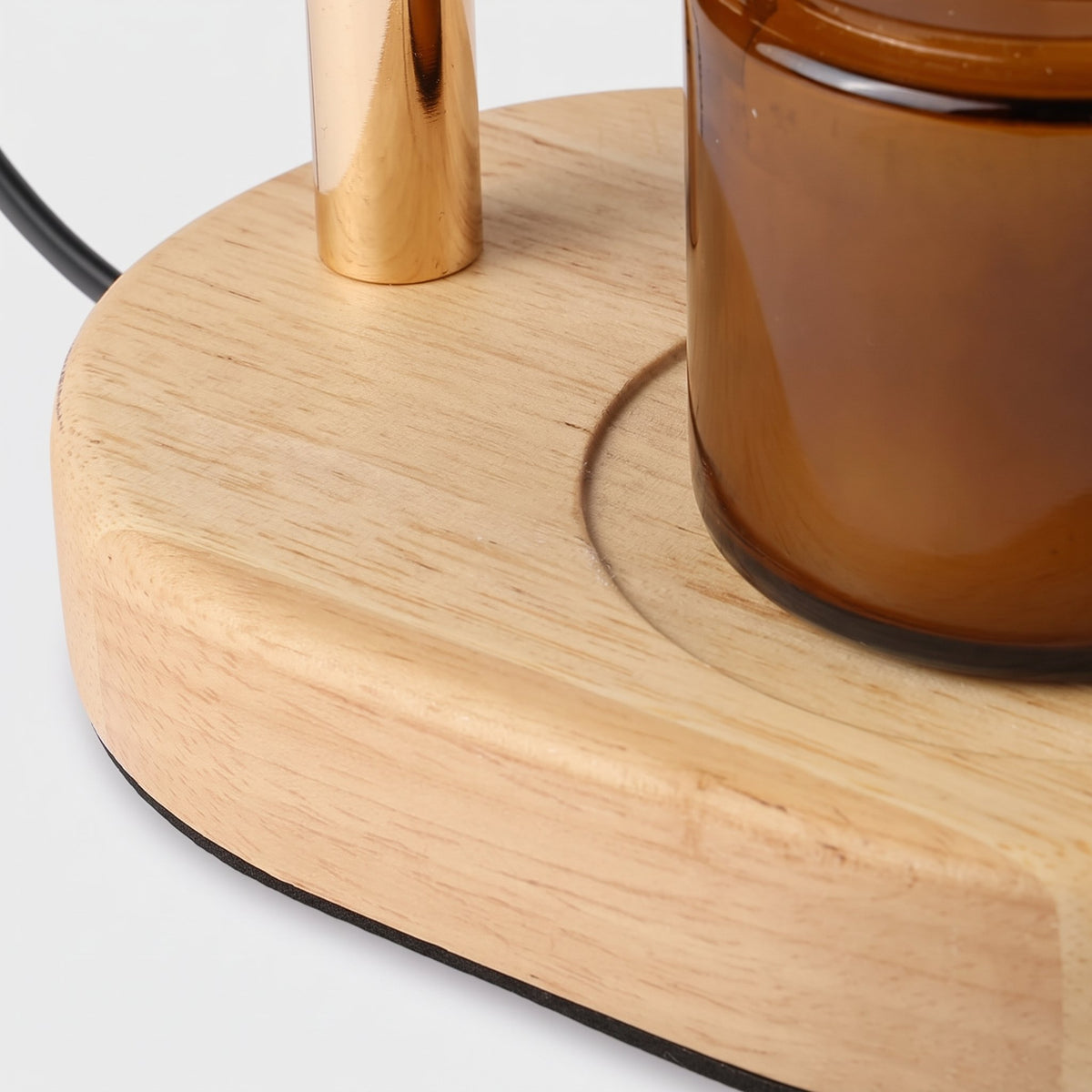 Close-up of the Ambra candle warmer lamp wooden base, gold-finish pole and amber candle jar on a light grey background