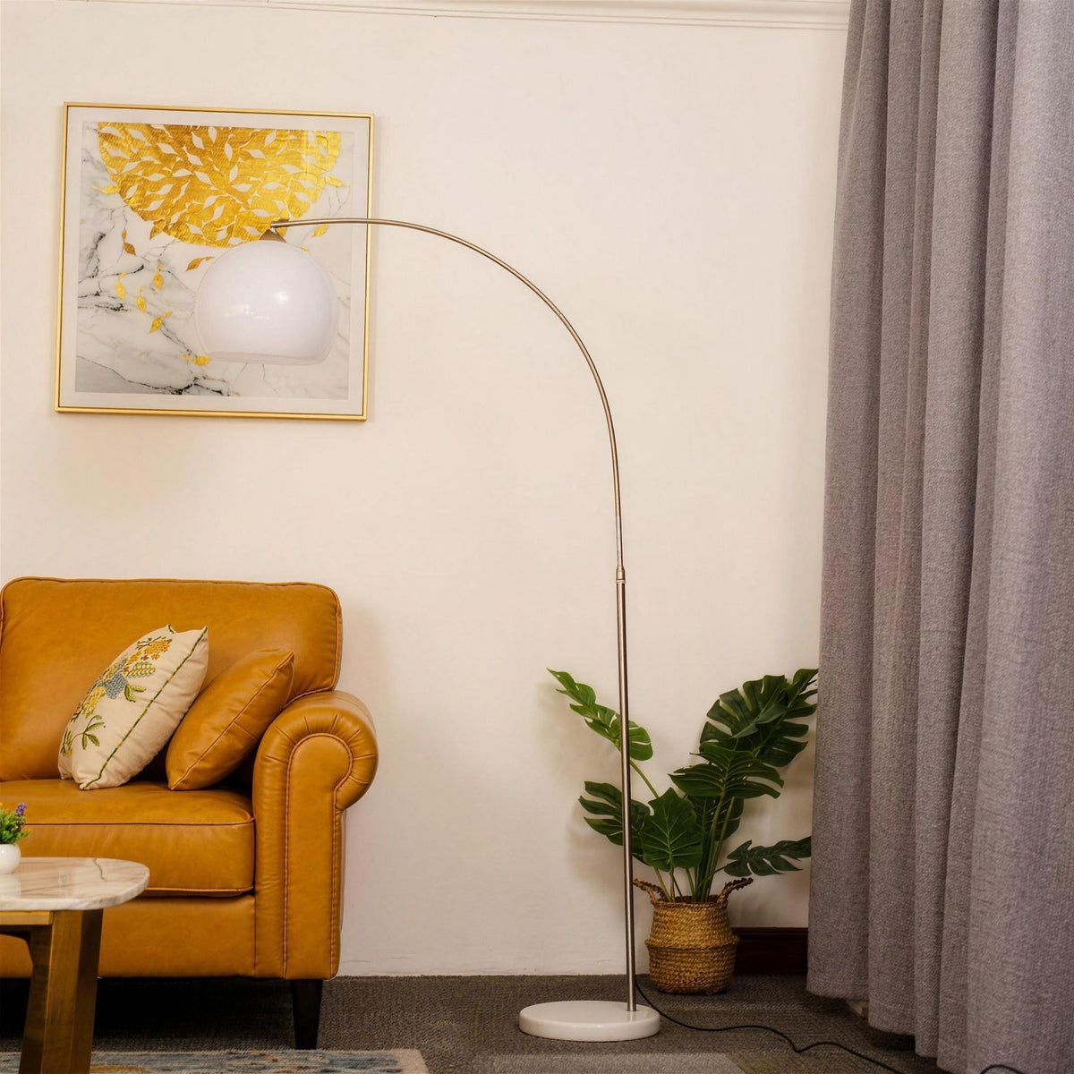 Ardo white arc floor lamp arching over a mustard yellow leather sofa in a cream living room with a plant