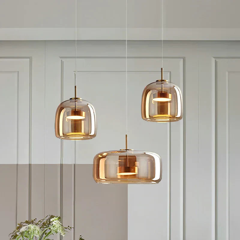 Cluster of three beqi amber glass pendant lights in various shapes suspended over a modern dining table