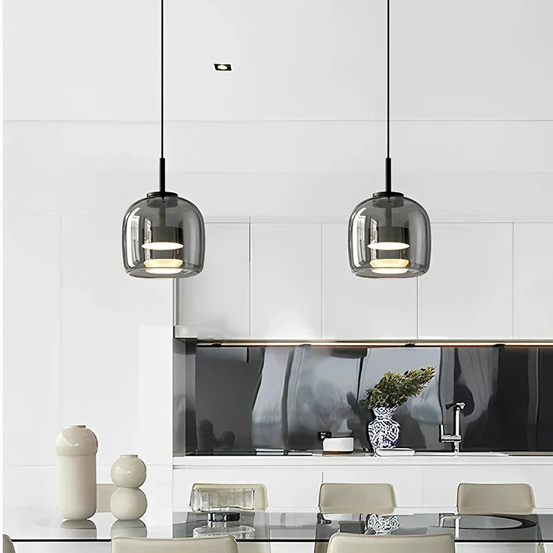 Pair of beqi smoke grey glass pendant lights hanging above a bright, minimalist white kitchen counter