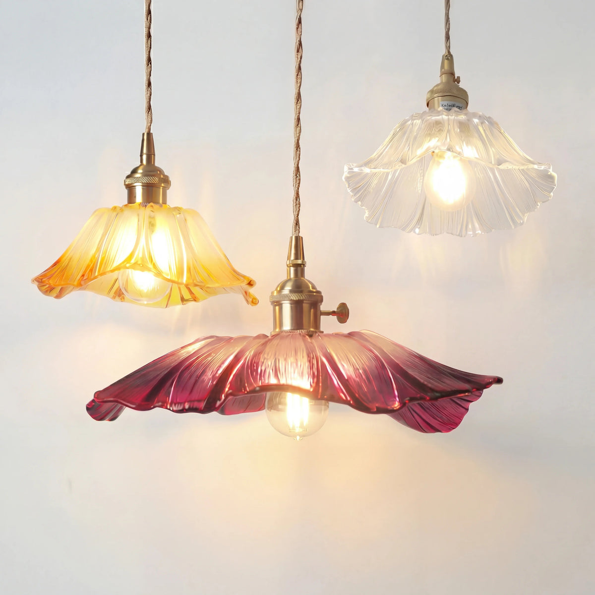Cluster of three retro floral glass bila pendants in yellow, purple, and clear illuminating together