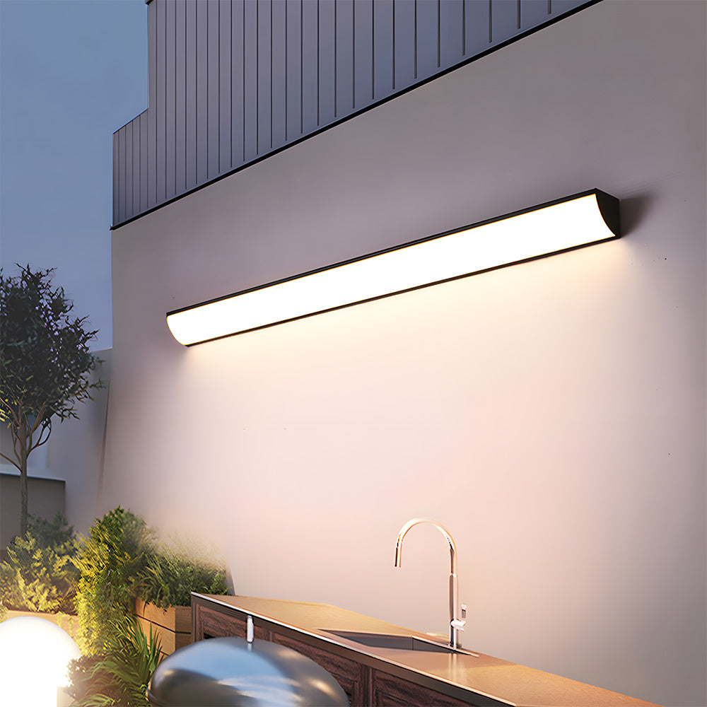 Long front-lit linear exterior bubce sconce illuminating a modern outdoor kitchen and patio area