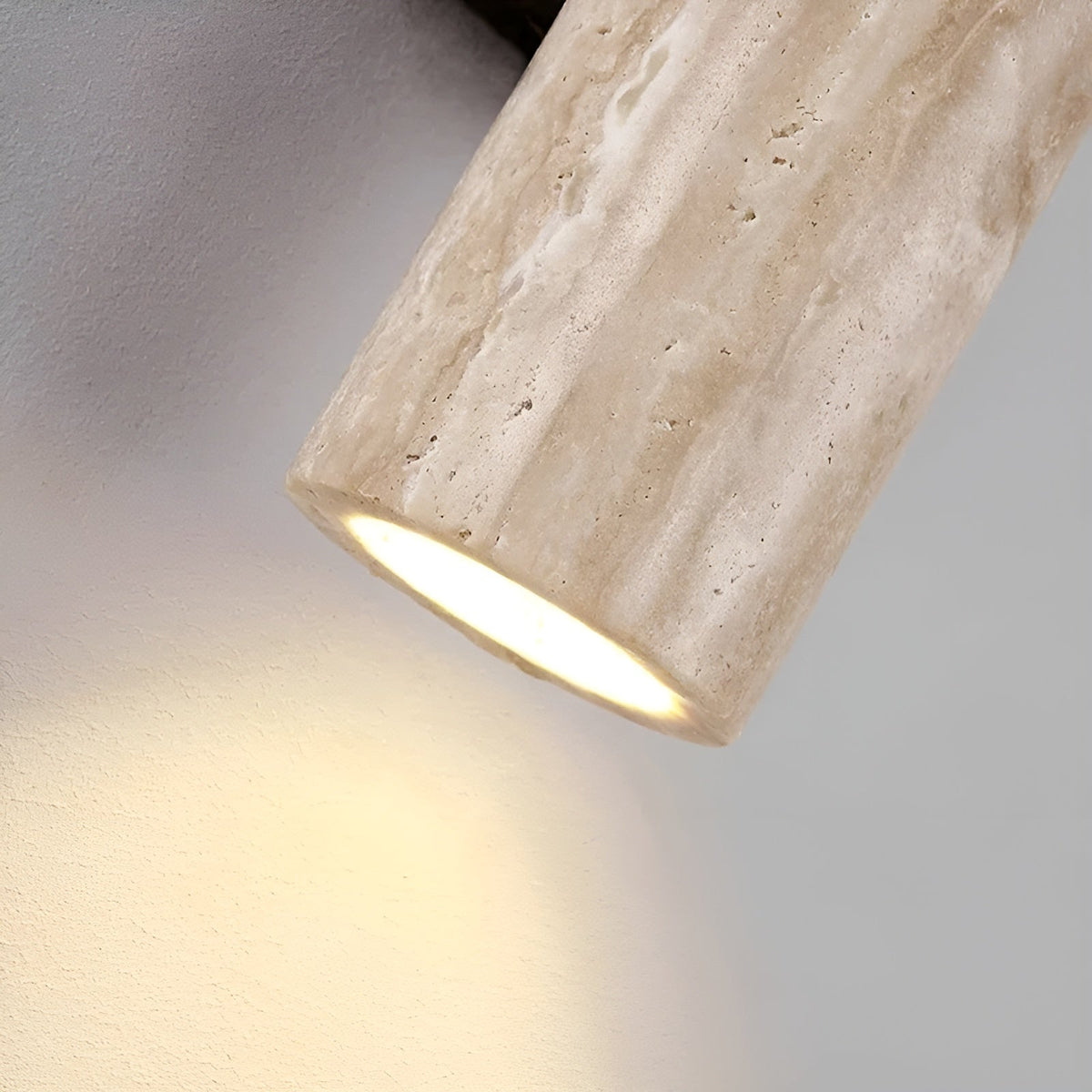 Close-up detail of the natural travertine bura wall sconce showing the warm LED light emitting from the bottom