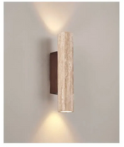 Modern cylindrical travertine bura wall sconce casting a warm up and down light on a plain wall