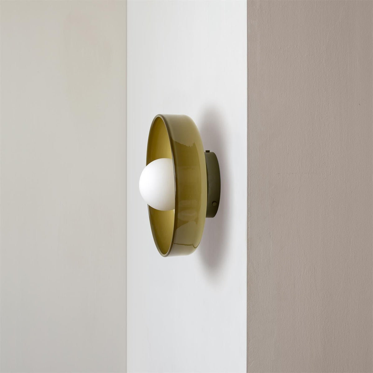 Olive green glass disc cenas wall light with a milky-white opal globe mounted on a white wall