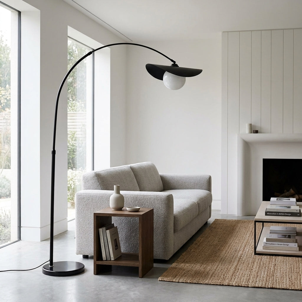 Clent black arc floor lamp arching over a light grey sofa beside a fireplace in a bright living room
