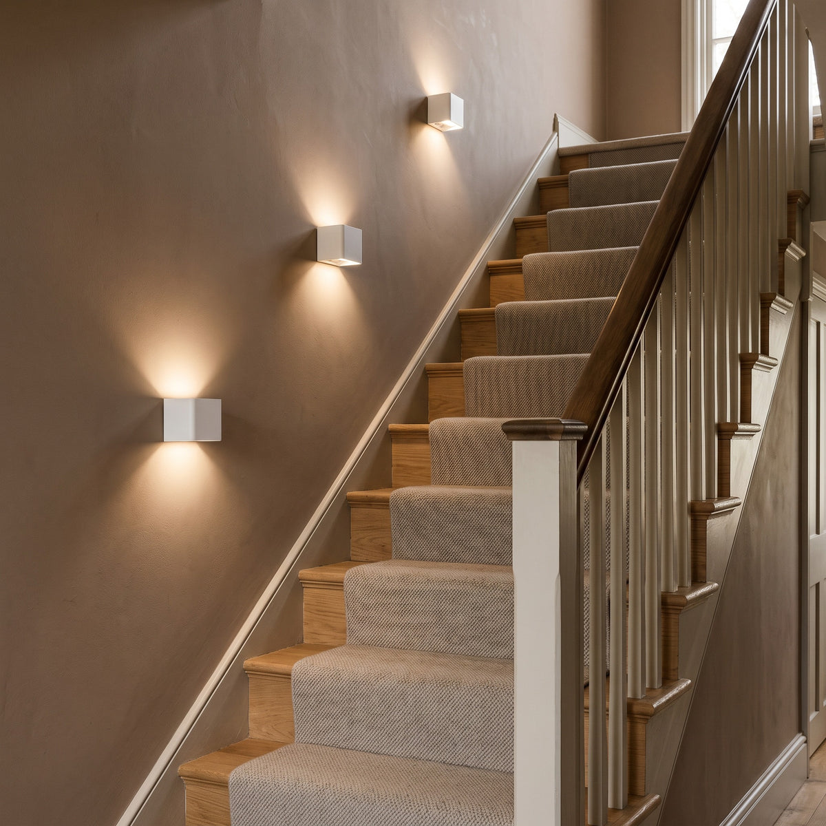 3 Cubo white cube wall lights in a diagonal line on a taupe staircase wall above a carpeted stair runner