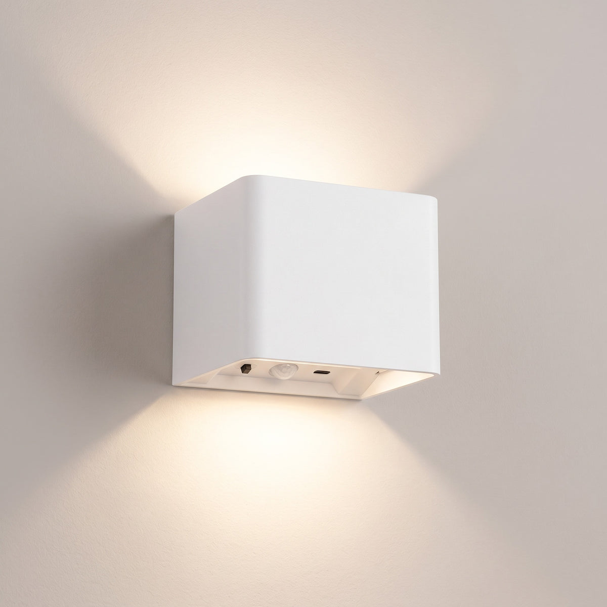 Cubo white cube wall light switched on, casting a soft up and down glow on a plain warm-grey wall