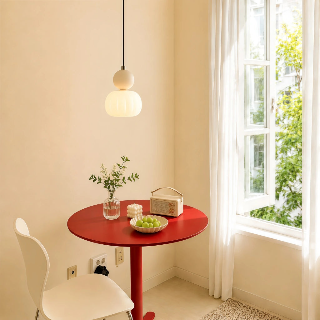 Beige debz geometric pendant light suspended over a small red dining table in a sunlit corner