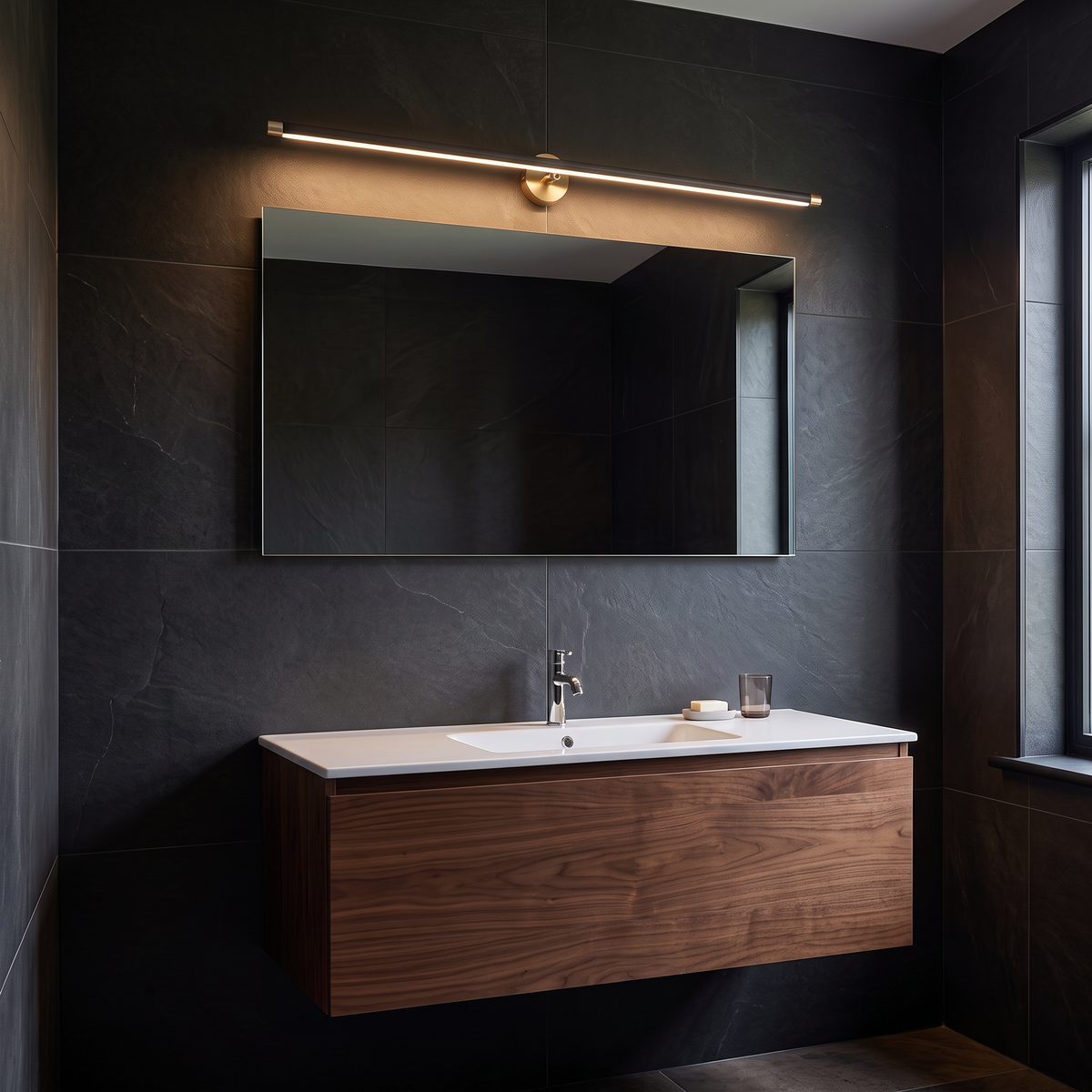 Doven black 98 cm linear LED wall light above a mirror and walnut floating vanity in a charcoal tiled British bathroom