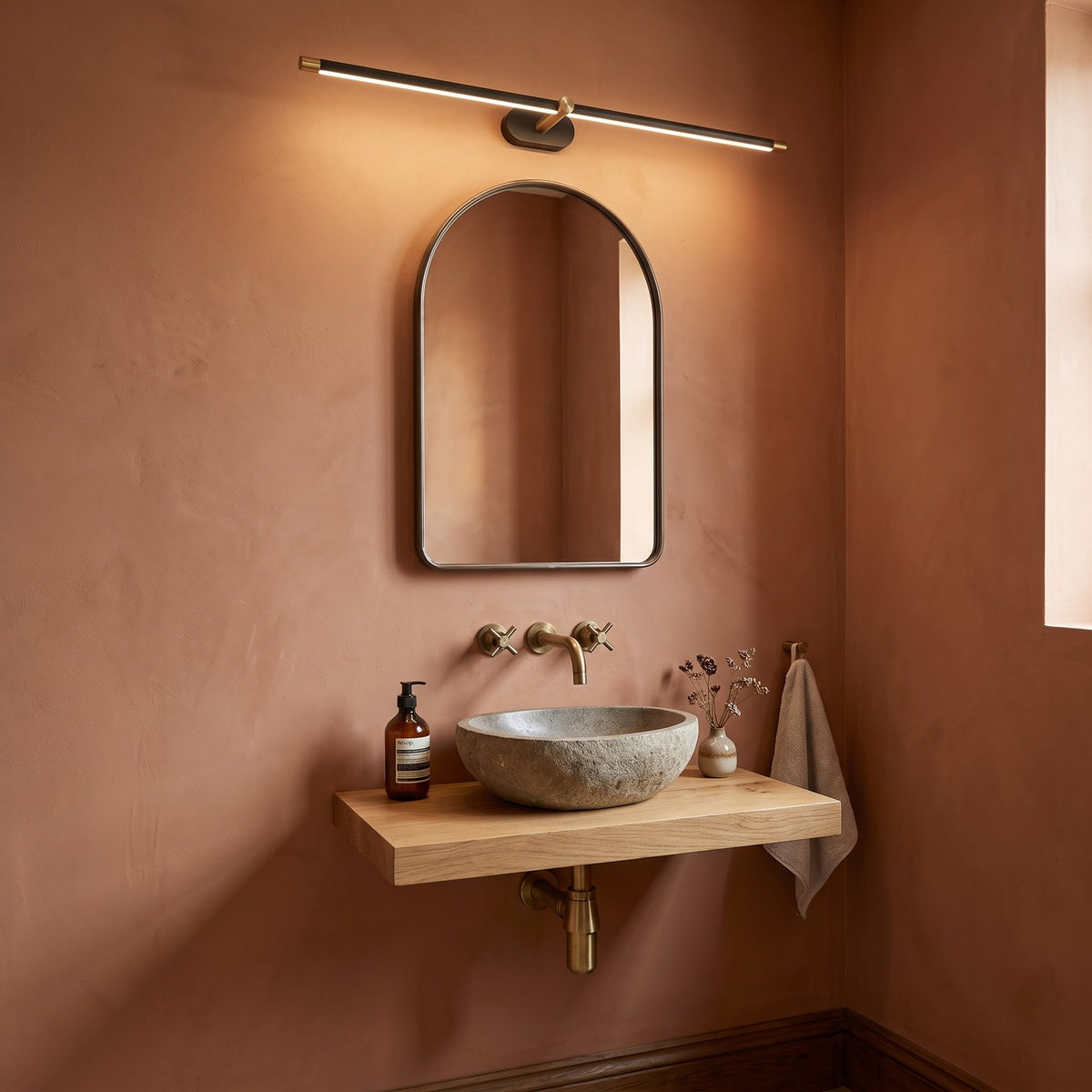 Doven black linear LED wall light above an arched mirror and stone basin in a terracotta British cloakroom