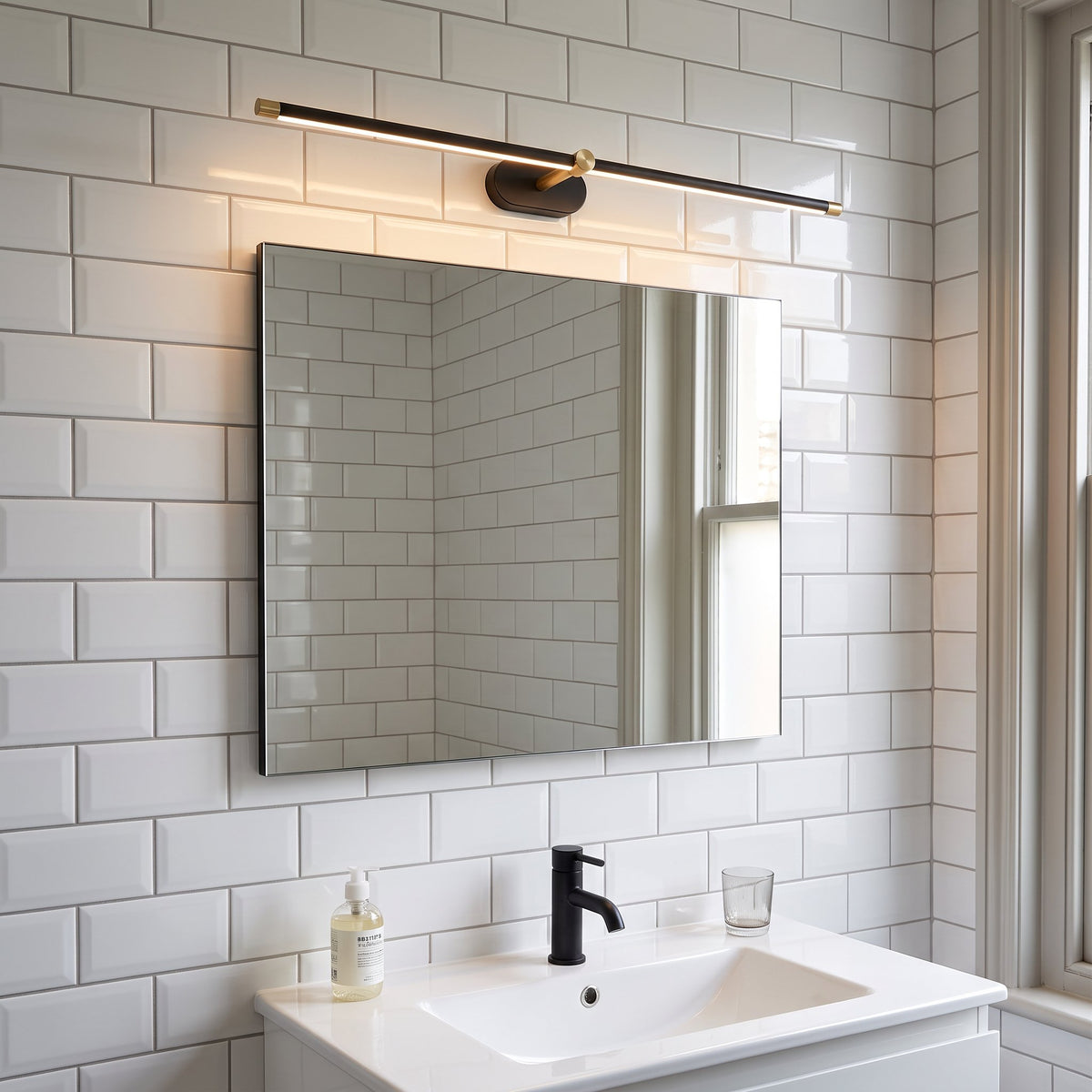Doven black linear LED wall light above a mirror in a British bathroom with white metro tiles