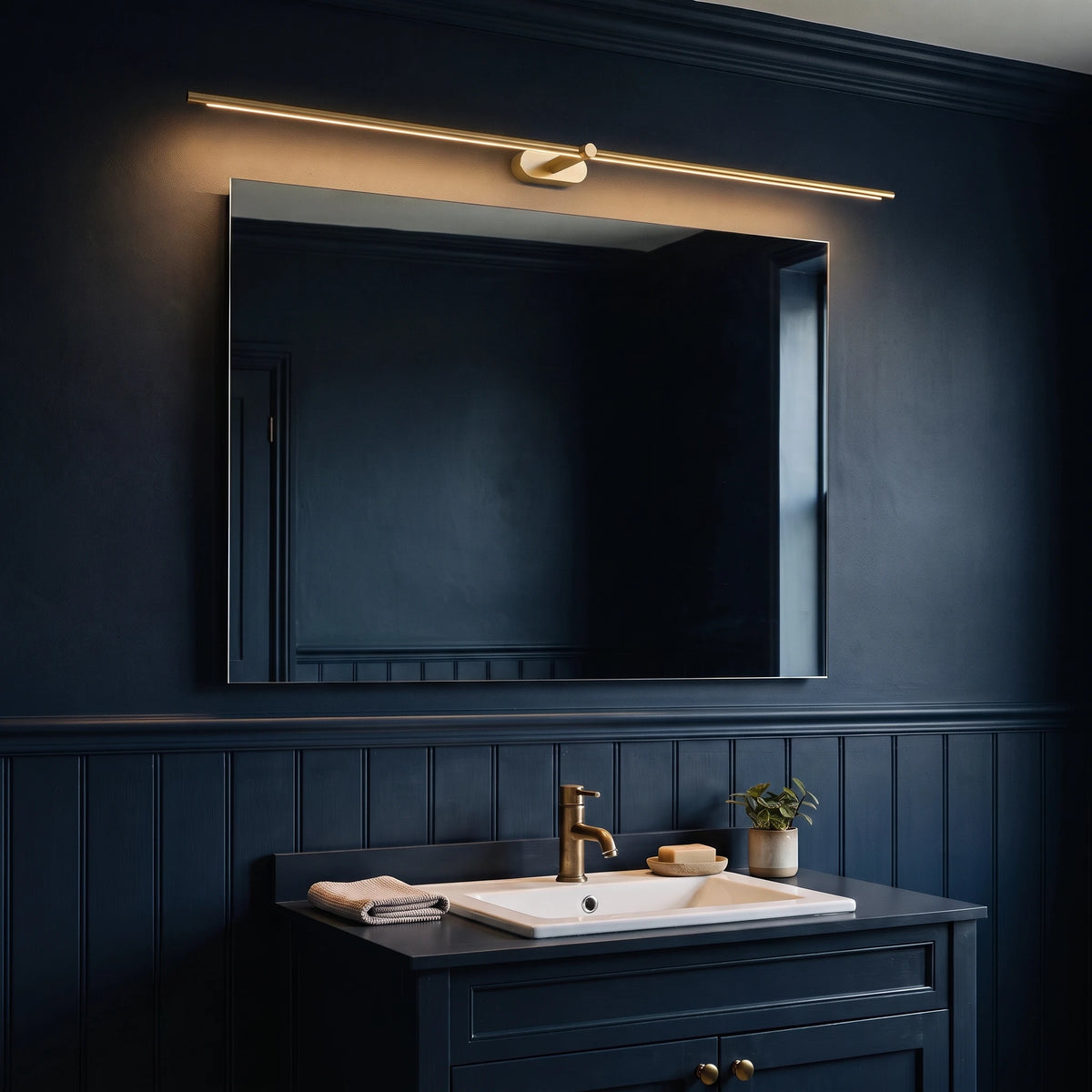 Doven gold-finish linear LED wall light above a mirror in a dark navy British bathroom