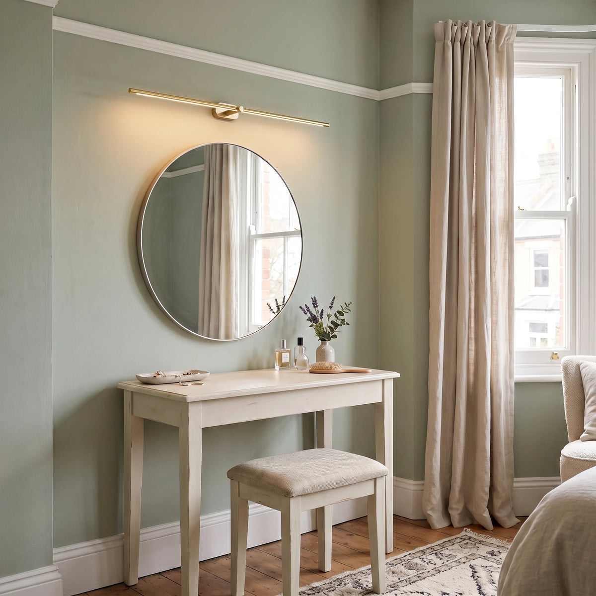 Doven gold-finish linear LED wall light above a round mirror and dressing table in a sage green British bedroom