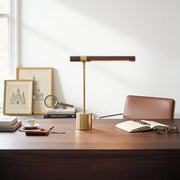Elkon walnut and brass T-bar LED desk lamp on a dark wood desk in a bright minimalist room