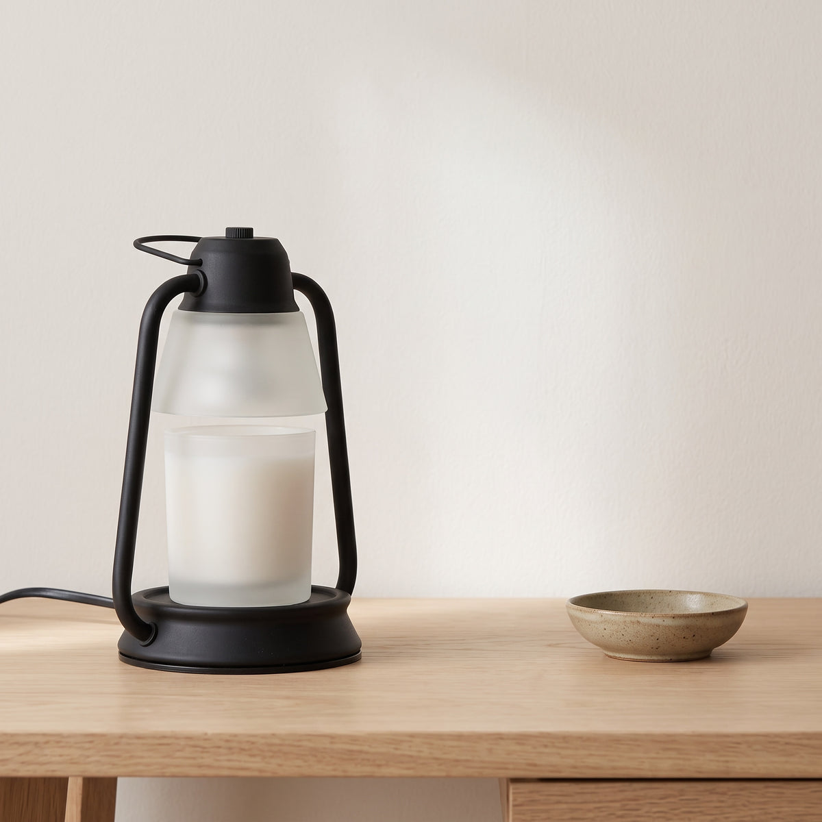 Embra black lantern candle warmer lamp with a frosted candle jar on an oak desk