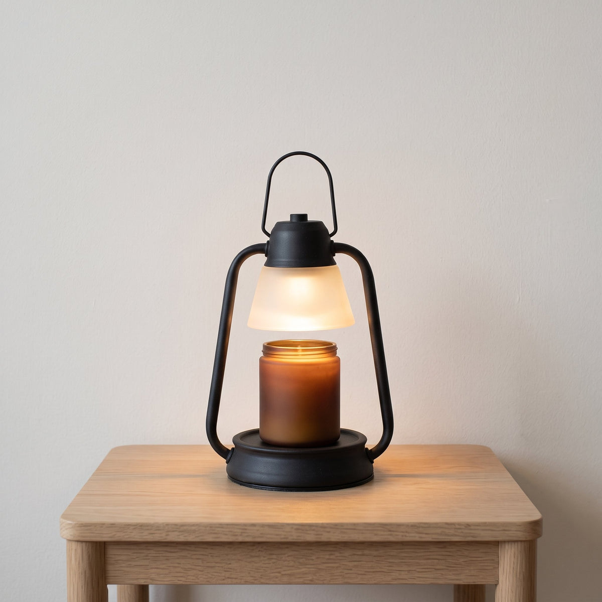 Embra black lantern candle warmer lamp glowing on an oak side table in a living room