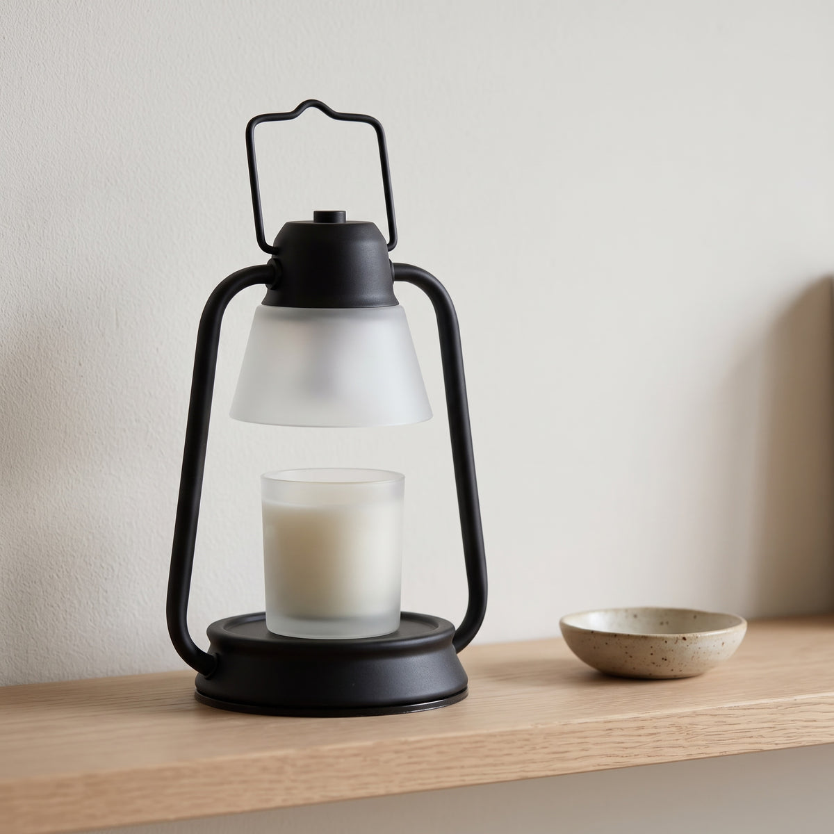 Embra black lantern candle warmer lamp on an oak shelf beside a small ceramic dish