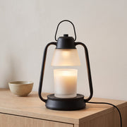 Embra black lantern candle warmer lamp with a frosted glass shade warming a candle jar on an oak sideboard
