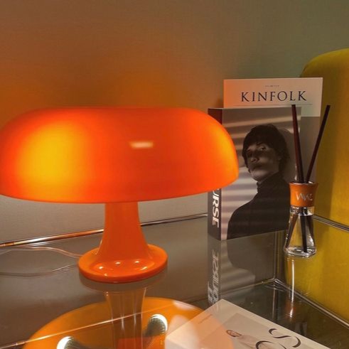 Glossy orange retro mushroom euter lamp glowing warmly on a glass shelf next to a Kinfolk book