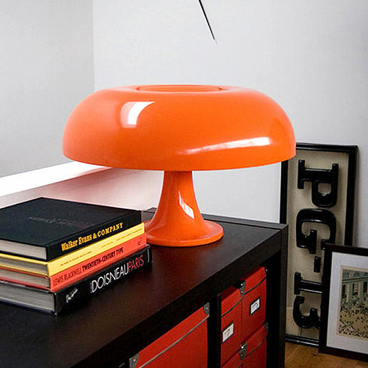 Orange 1970s style mushroom euter table lamp resting elegantly on a black cabinet with stacked books
