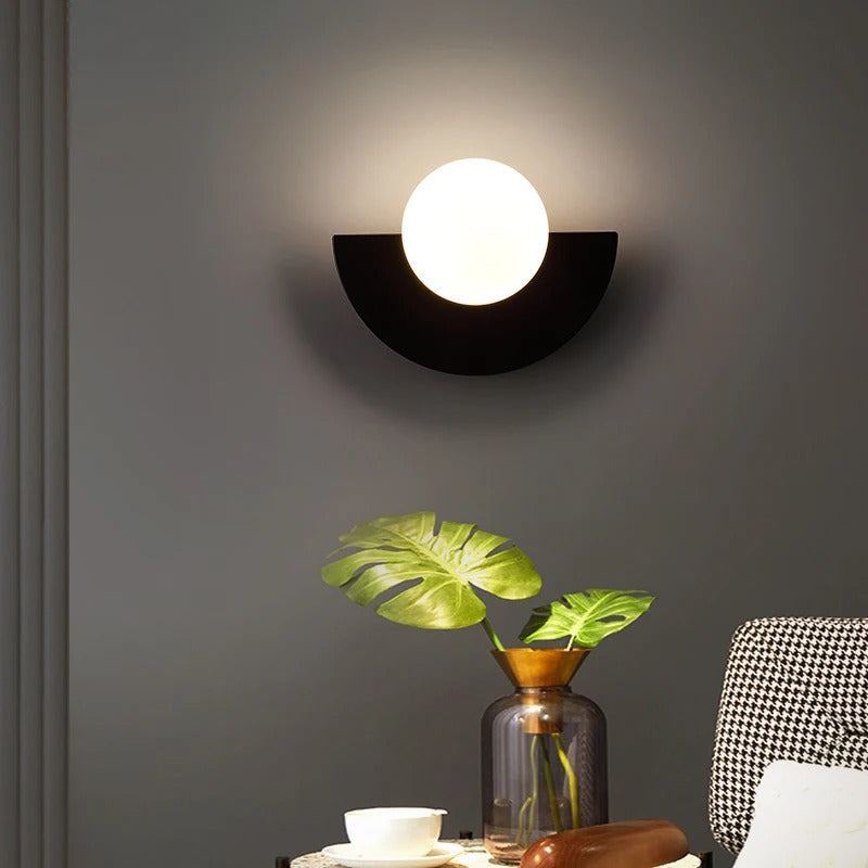 Black minimalist globe fers wall light casting a soft, glare-free ambient glow over a decorated side table