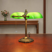 Close view of the Gemma green glass bankers lamp on a wooden table beside a small vase of flowers