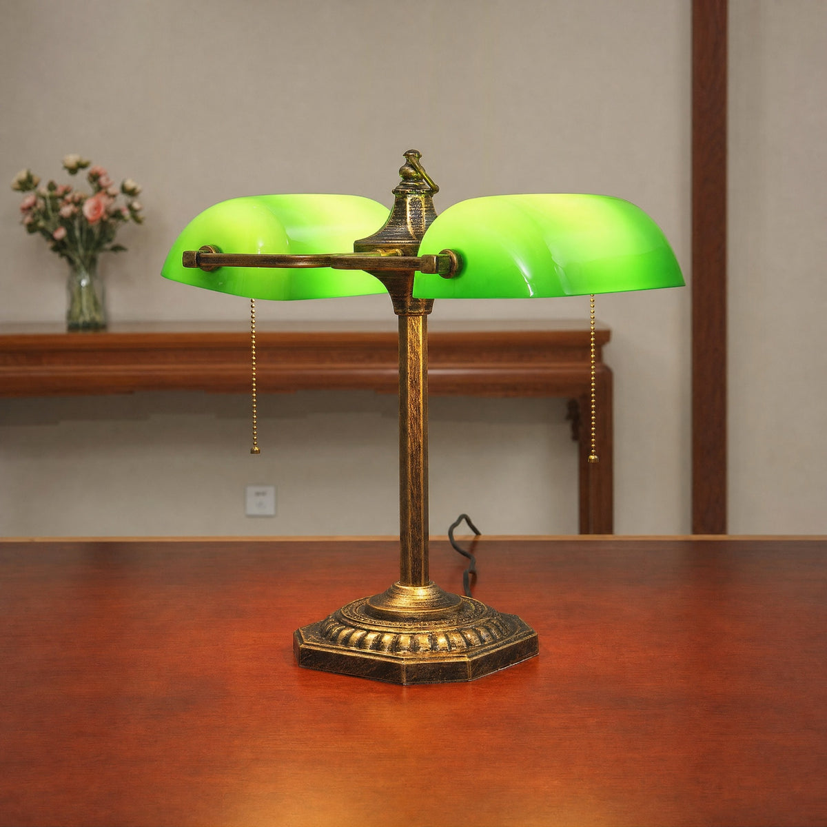 Close view of the Gemma green glass bankers lamp on a wooden table beside a small vase of flowers
