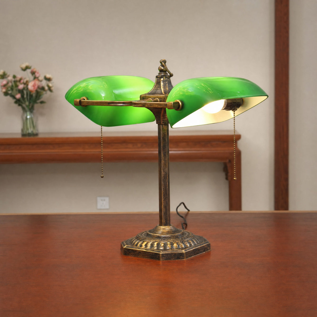 Gemma green glass double bankers lamp on a wooden table with a small vase of flowers behind