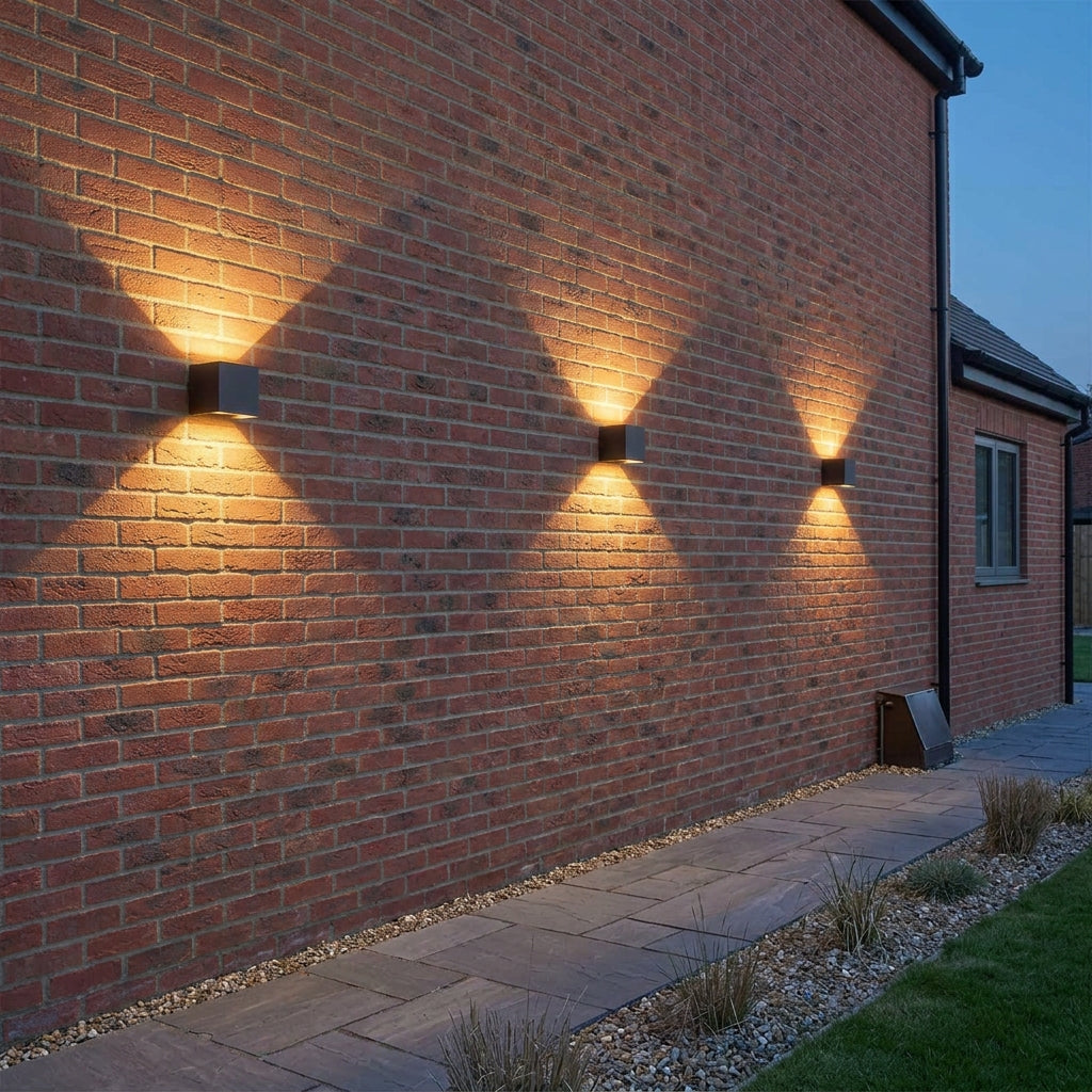 Row of three Glim black up and down outdoor wall lights grazing a red brick wall with warm white light
