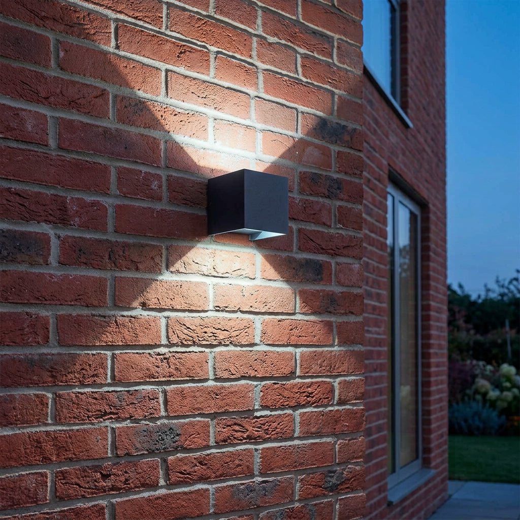 Glim black square up and down LED outdoor wall light in cool white on a red brick wall at dusk