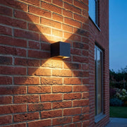 Glim black square up and down LED outdoor wall light in warm white on a red brick wall at dusk