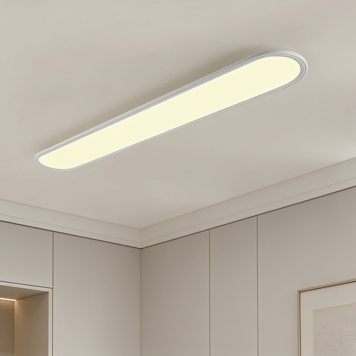 Grale white oval linear LED ceiling light glowing warm white in a room with cornice and cupboards