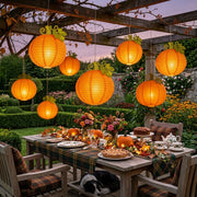 Harvest pumpkin paper lanterns lit over a garden dinner table at dusk