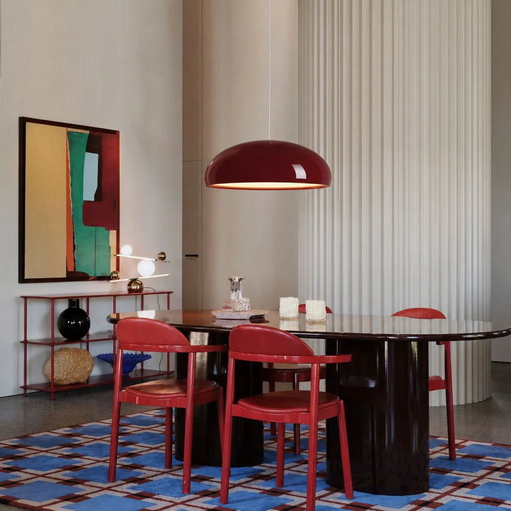 Red Nordic huhs pendant light providing a warm glare-free glow over a dark dining table