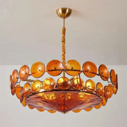 Joltly amber glass disc chandelier hanging from a gold-finish ceiling canopy against a plain grey wall