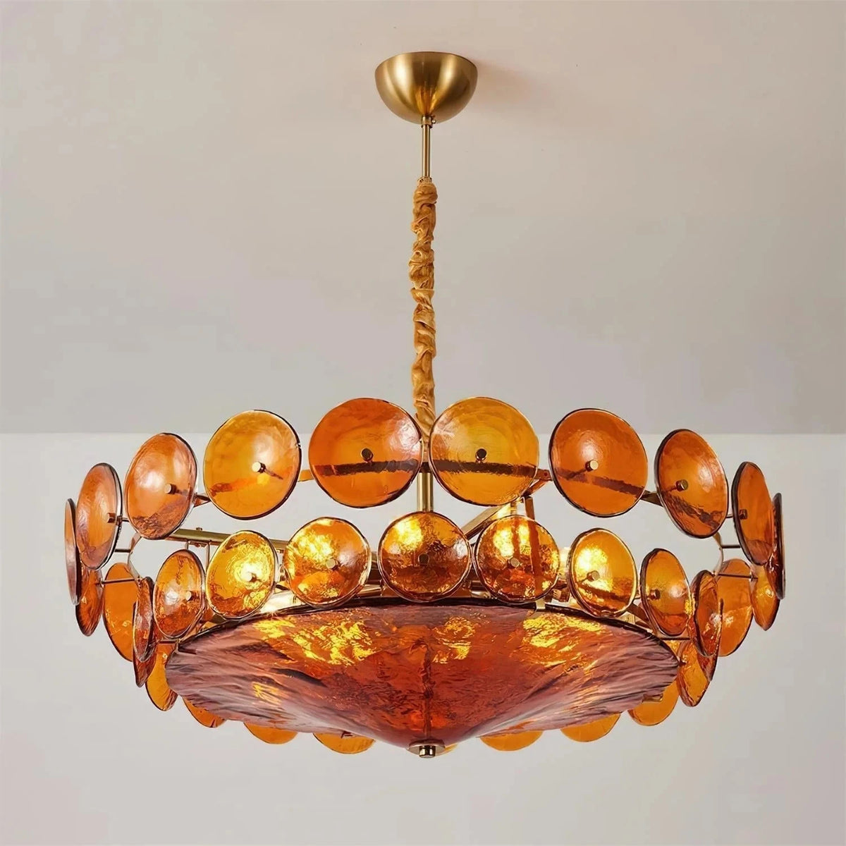 Joltly amber glass disc chandelier hanging from a gold-finish ceiling canopy against a plain grey wall