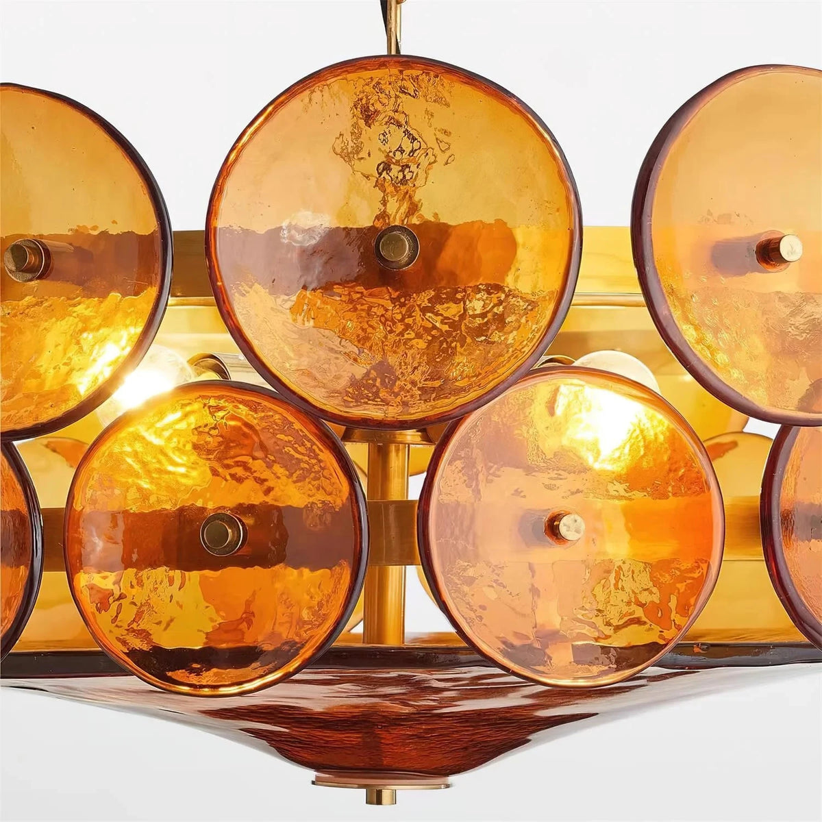 Close-up of the lit amber glass discs and gold-finish frame of the Joltly chandelier