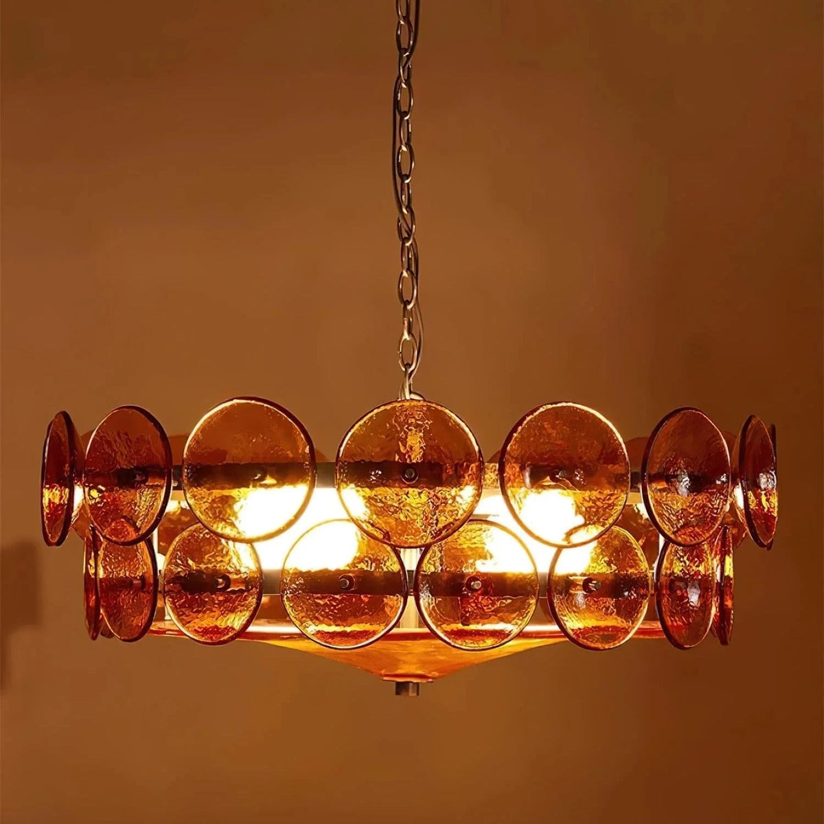 Joltly amber glass disc chandelier lit against a warm brown wall