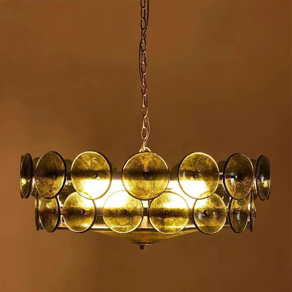 Joltly green glass disc chandelier lit against a warm brown wall