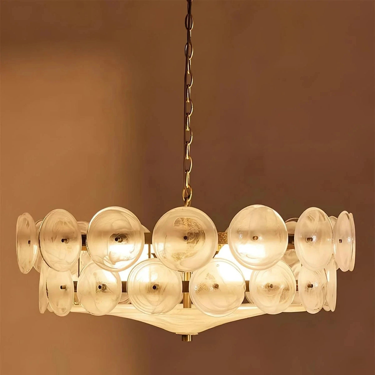 Joltly white frosted glass disc chandelier lit against a warm brown wall