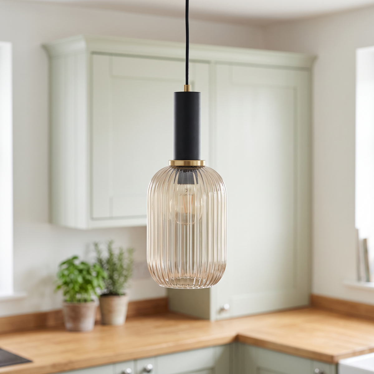 Kael champagne ribbed glass cylinder pendant light with a black cap and thin brass ring in front of sage green kitchen cabinets