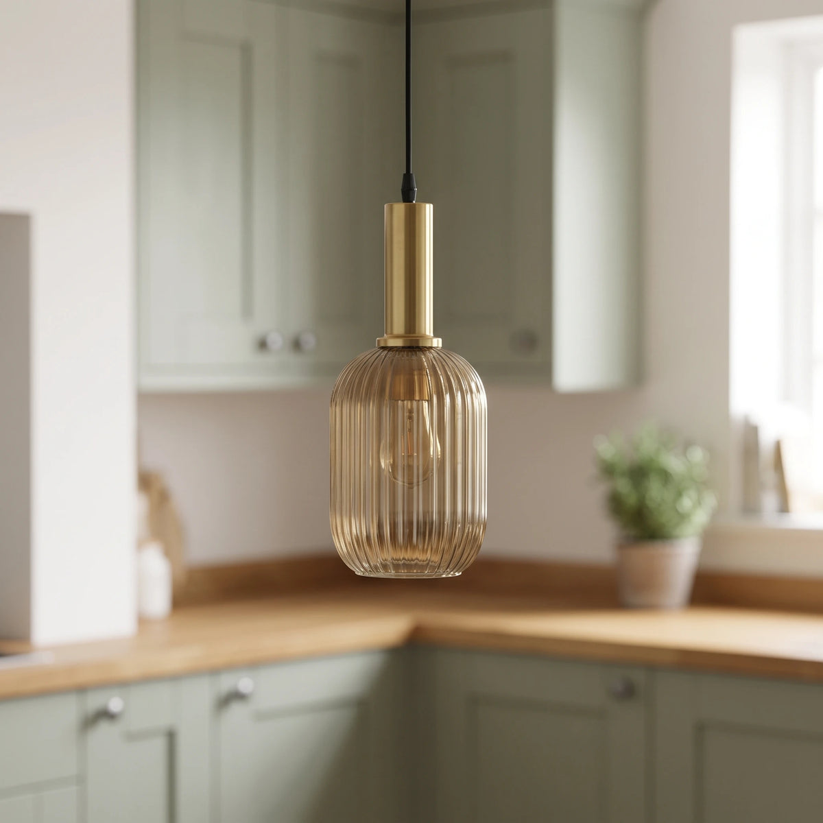 Kael champagne ribbed glass cylinder pendant light with a brass cap in front of sage green kitchen cabinets