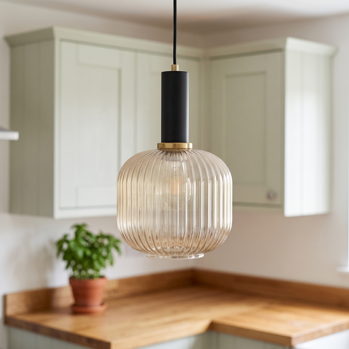 Kael champagne ribbed glass jar pendant light with a black cap and thin brass ring in front of sage green kitchen cabinets