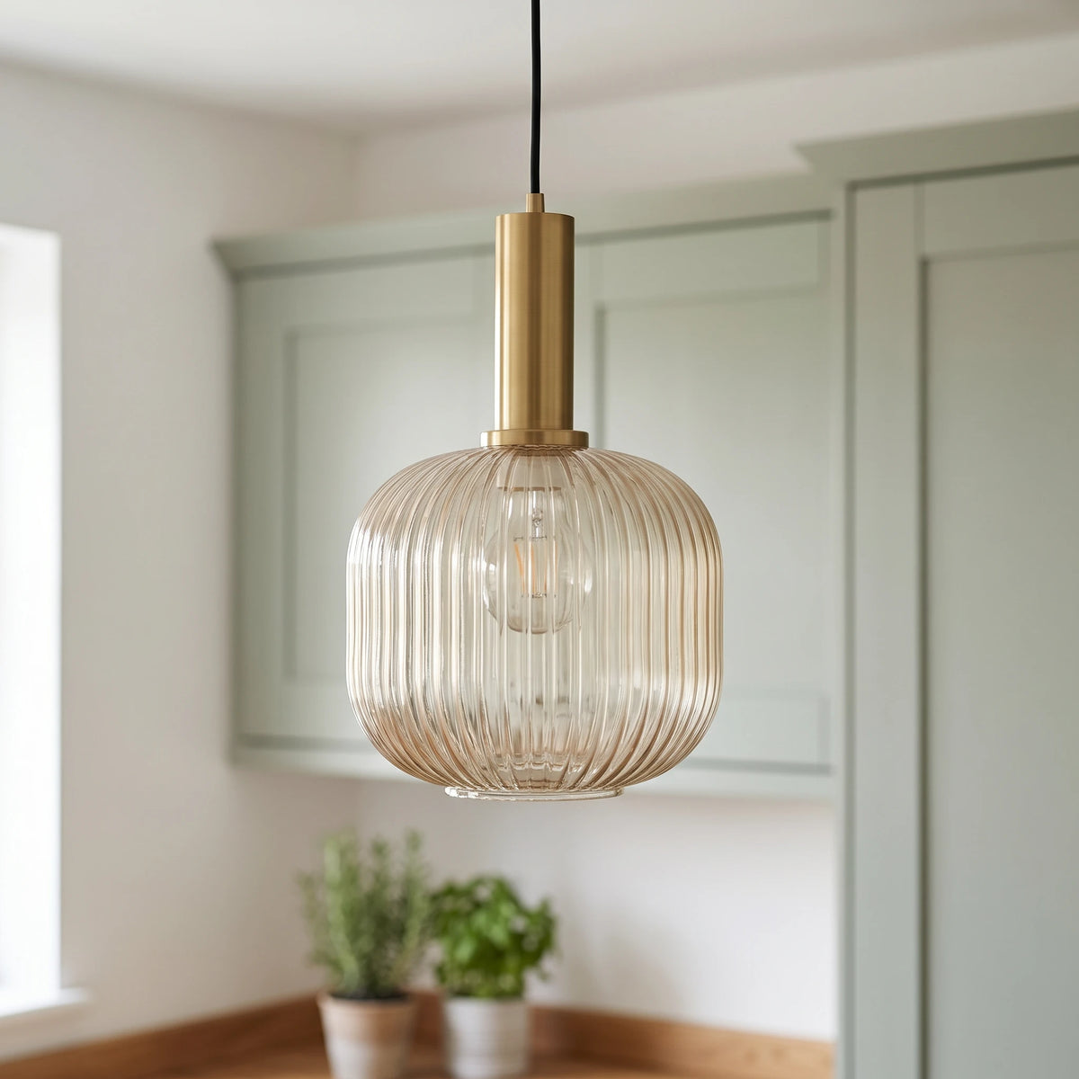 Kael champagne ribbed glass jar pendant light with a brass cap in front of sage green kitchen cabinets