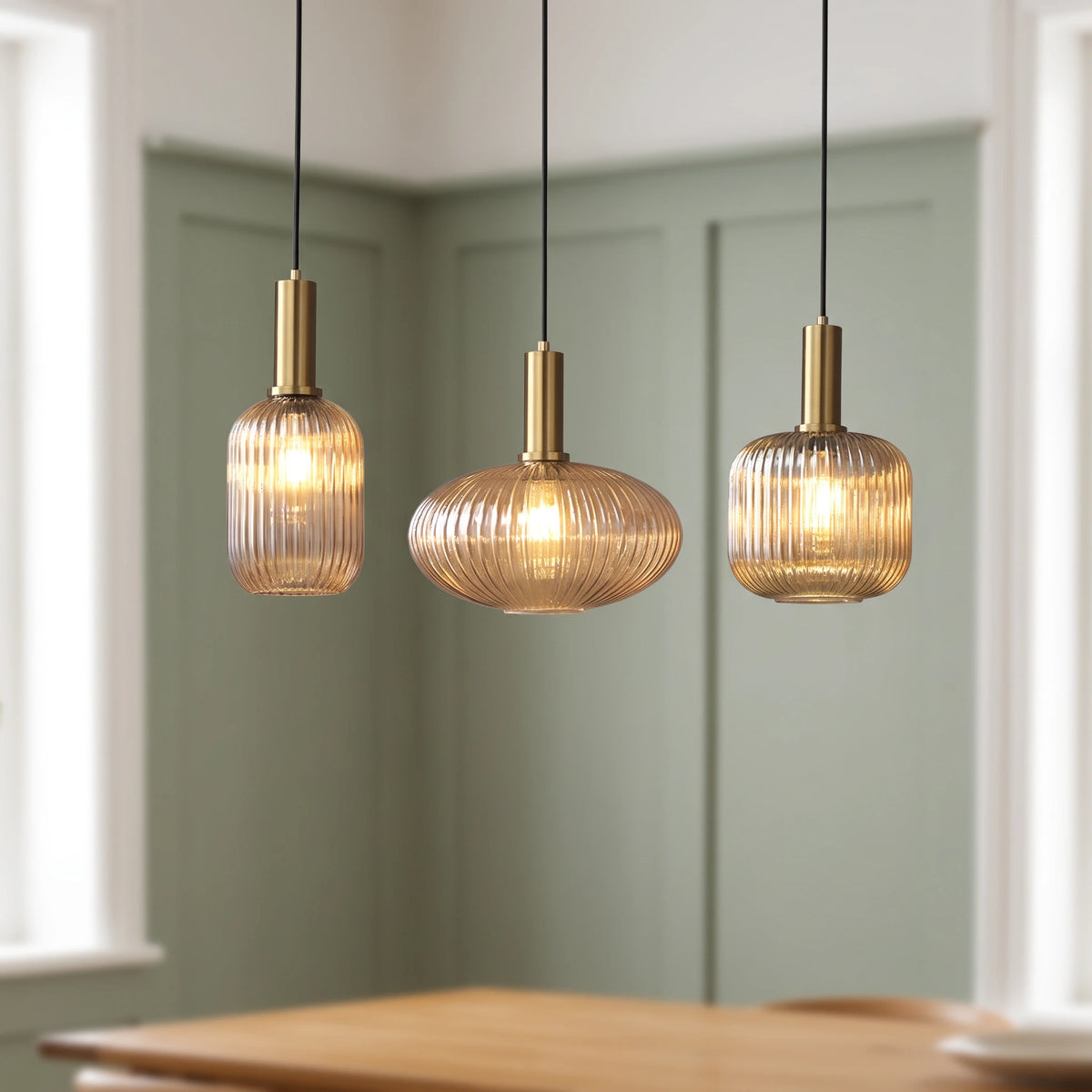 3 Kael champagne ribbed glass pendant lights with brass caps above a dining table in a sage green panelled room